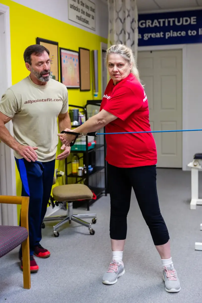 Tim coaching a client in her 60s through a resistance-band row, his hand guiding her elbow