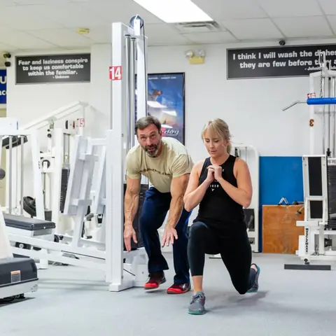 Tim crouched beside a client to check her lunge form