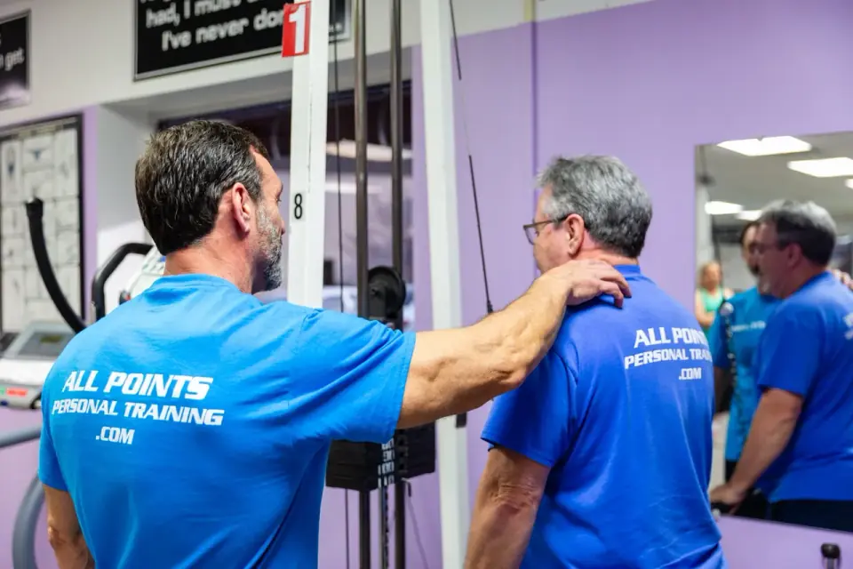 Tim with his hand on a client's shoulder, cueing posture at a cable machine